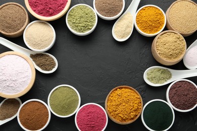 Photo of Frame of different superfood powders in bowls and spoons on dark textured table, flat lay. Space for text