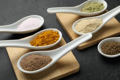 Photo of Different superfood powders in spoons on dark textured table, closeup