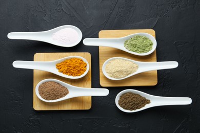 Photo of Different superfood powders in spoons on dark textured table, flat lay