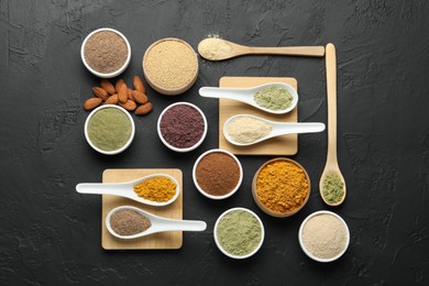 Photo of Different superfood powders in spoons and bowls on dark textured table, flat lay