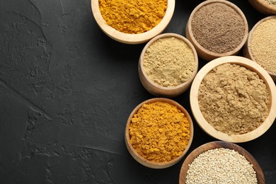 Photo of Different superfood powders in bowls on dark textured table, flat lay. Space for text