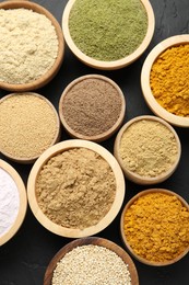 Photo of Different superfood powders in bowls on dark textured table, flat lay