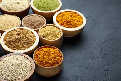 Photo of Different superfood powders in bowls on dark textured table, closeup. Space for text
