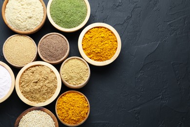 Photo of Different superfood powders in bowls on dark textured table, flat lay. Space for text