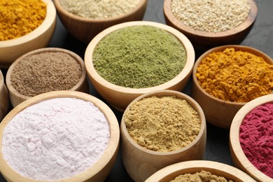 Photo of Different superfood powders in bowls on dark table, closeup