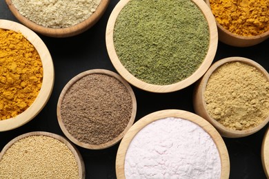 Photo of Different superfood powders in bowls on dark table, flat lay