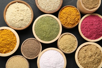 Photo of Different superfood powders in bowls on dark textured table, flat lay