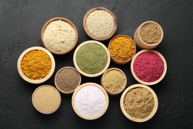 Photo of Different superfood powders in bowls on dark textured table, flat lay