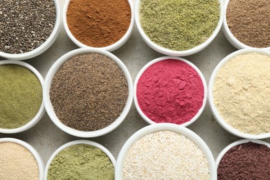 Photo of Different superfood powders in bowls on grey textured table, flat lay