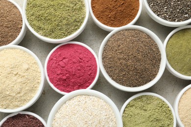 Photo of Different superfood powders in bowls on grey textured table, flat lay
