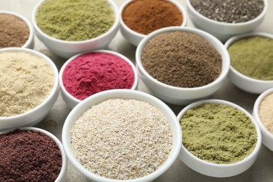 Photo of Different superfood powders in bowls on grey textured table, closeup