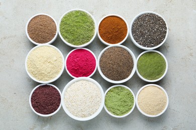 Photo of Different superfood powders in bowls on grey textured table, flat lay