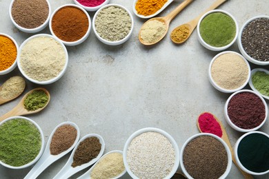 Photo of Frame of different superfood powders in bowls and spoons on grey textured table, flat lay. Space for text