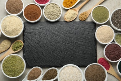 Photo of Different superfood powders and slate board on grey textured table, flat lay. Space for text