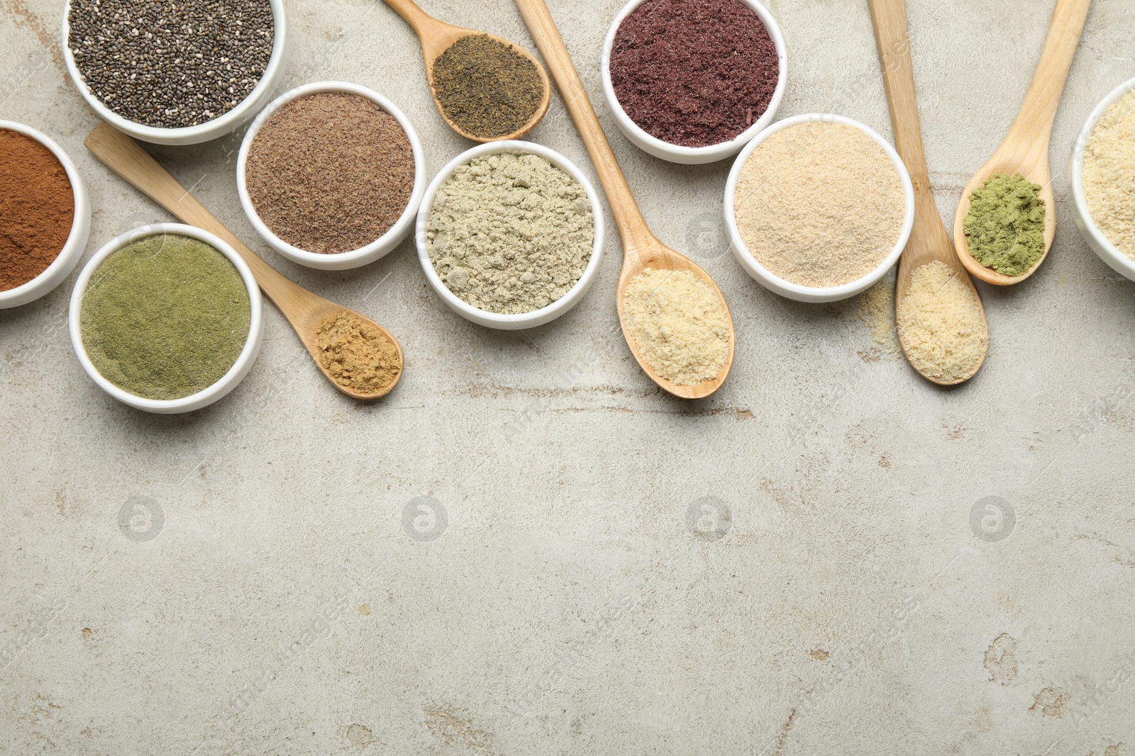 Different superfood powders in spoons and bowls on grey textured table, flat lay. Space for text Photo of Different superfood powders in spoons and bowls on grey textured table, flat lay. Space for text