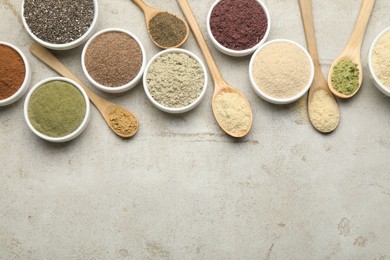 Photo of Different superfood powders in spoons and bowls on grey textured table, flat lay. Space for text