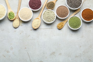 Photo of Different superfood powders in spoons and bowls on grey textured table, flat lay. Space for text