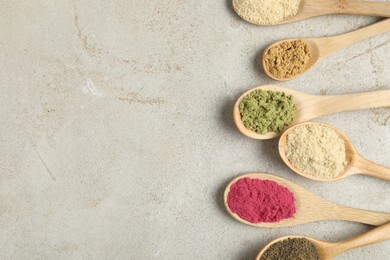 Photo of Different superfood powders in spoons on grey textured table, flat lay. Space for text