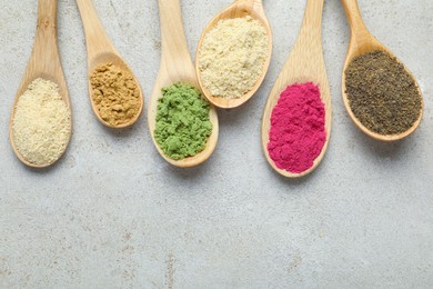 Photo of Different superfood powders in spoons on grey textured table, flat lay. Space for text