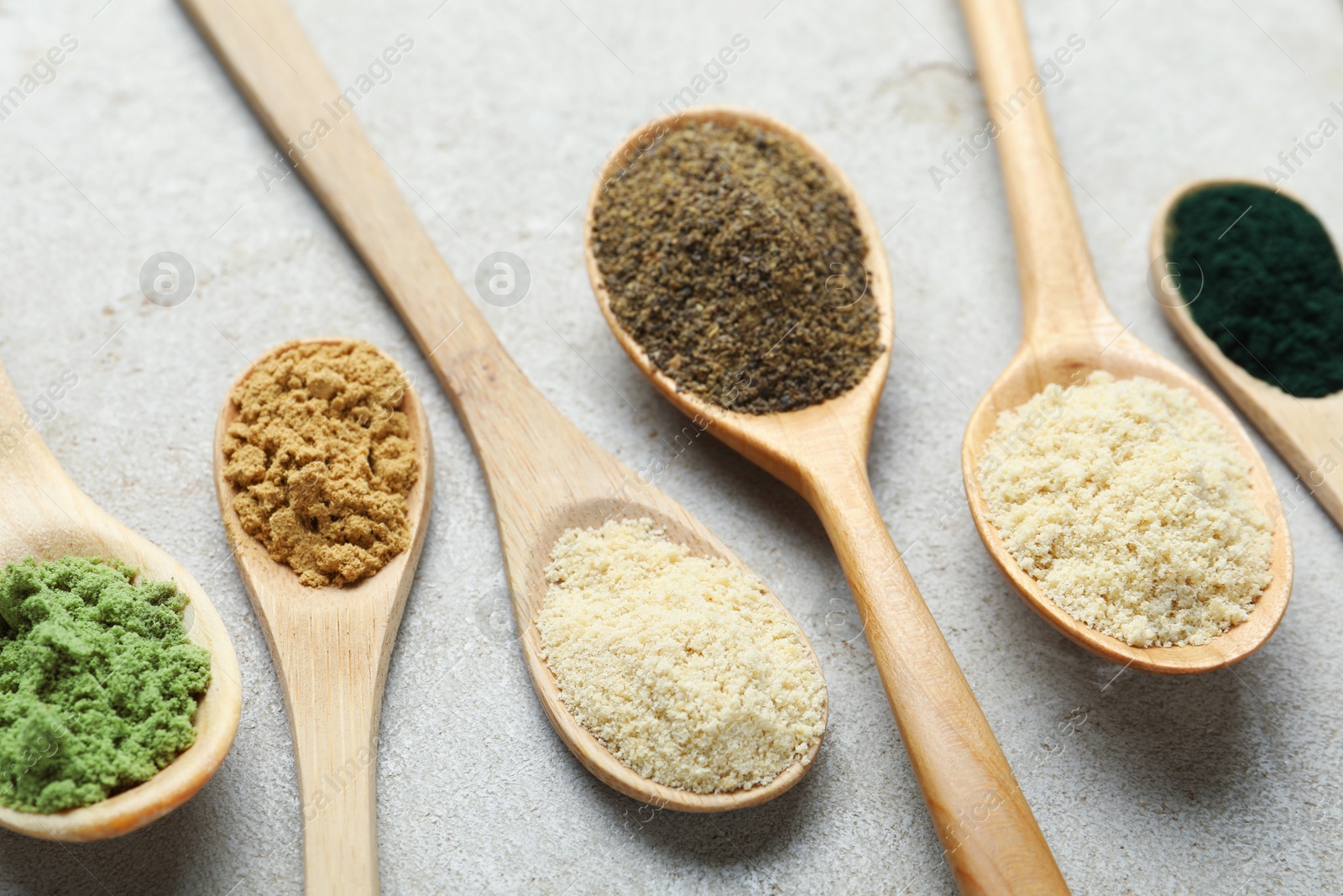 Different superfood powders in spoons on grey textured table, closeup Photo of Different superfood powders in spoons on grey textured table, closeup