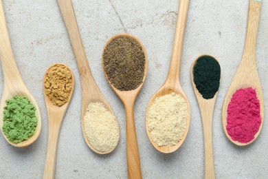 Photo of Different superfood powders in spoons on grey textured table, flat lay