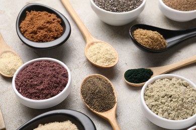 Photo of Different superfood powders in spoons and bowls on grey textured table