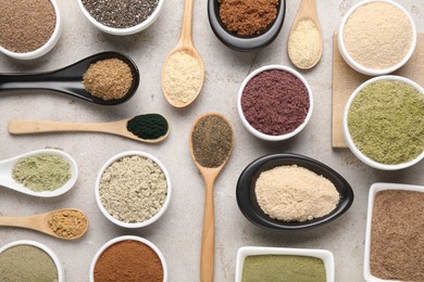 Photo of Different superfood powders in spoons and bowls on grey textured table, flat lay