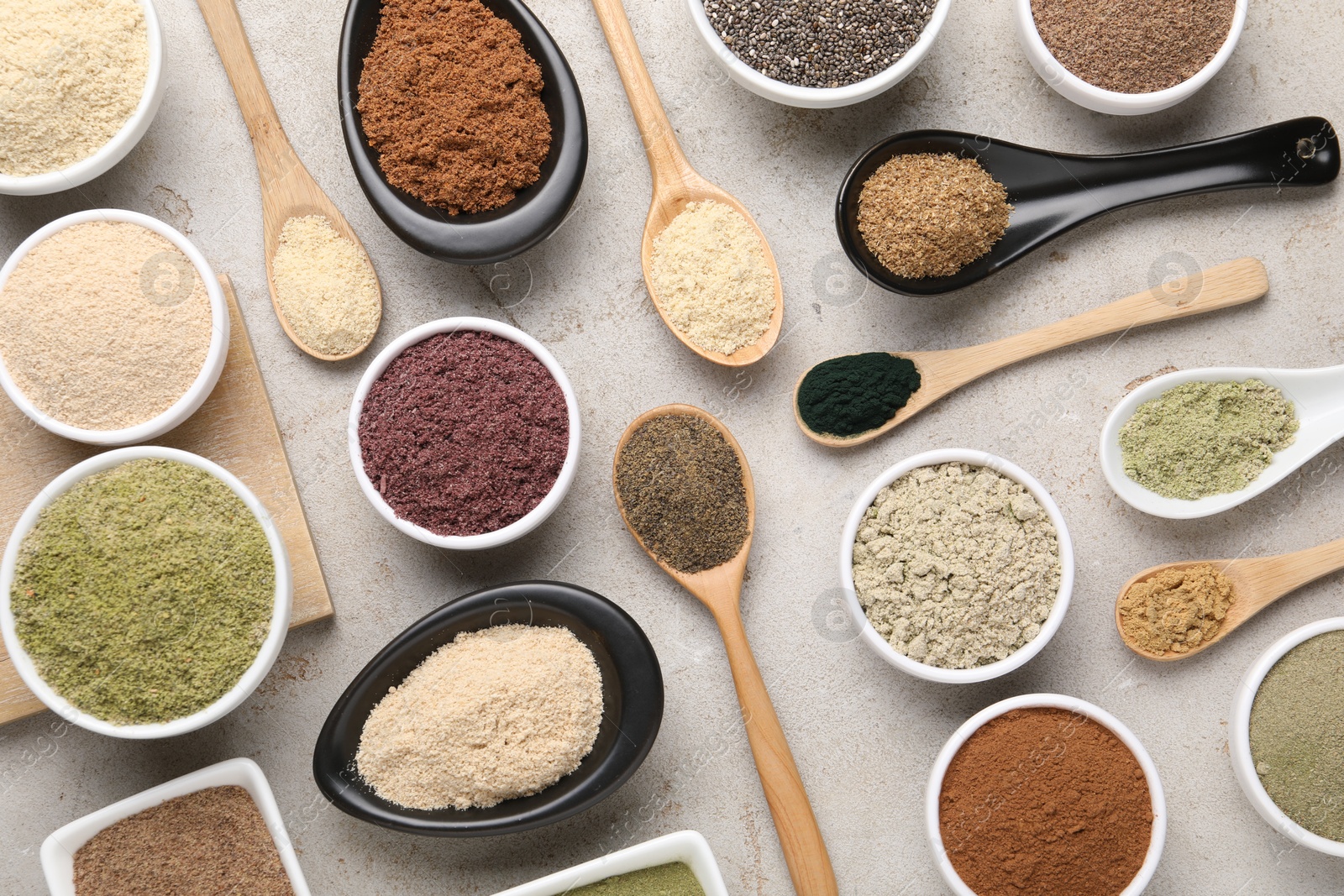Different superfood powders in spoons and bowls on grey textured table, flat lay Photo of Different superfood powders in spoons and bowls on grey textured table, flat lay