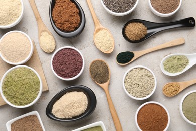 Photo of Different superfood powders in spoons and bowls on grey textured table, flat lay