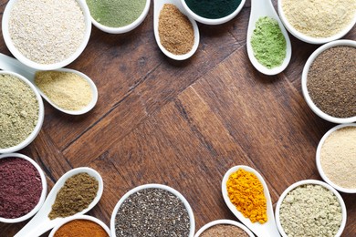 Photo of Frame of different superfood powders in bowls and spoons on wooden table, flat lay. Space for text