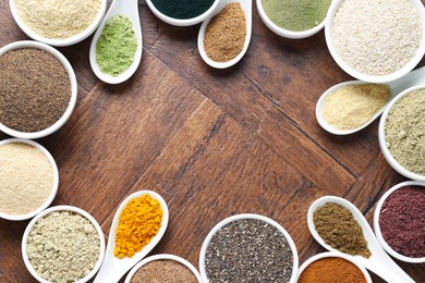 Photo of Frame of different superfood powders in bowls and spoons on wooden table, flat lay. Space for text