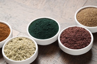 Photo of Different superfood powders in bowls on wooden table, closeup