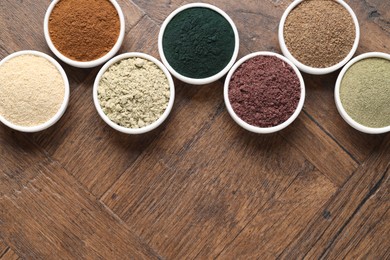 Photo of Different superfood powders in bowls on wooden table, flat lay. Space for text