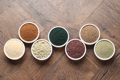 Photo of Different superfood powders in bowls on wooden table, flat lay