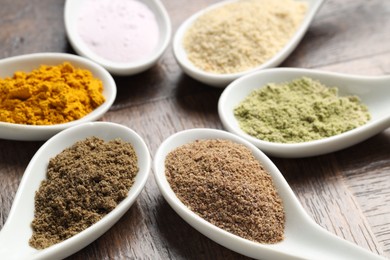 Photo of Different superfood powders in spoons on wooden table, closeup