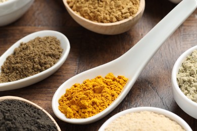 Photo of Different superfood powders in bowls and spoons on wooden table, closeup