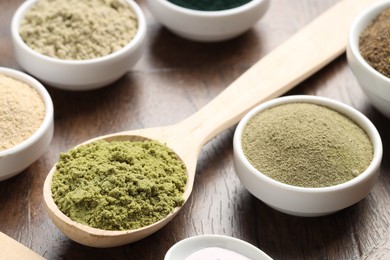 Photo of Different superfood powders in bowls and spoons on wooden table, closeup