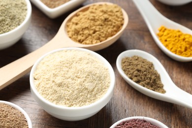 Photo of Different superfood powders in bowls and spoons on wooden table, closeup
