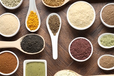 Photo of Different superfood powders in bowls and spoons on wooden table, flat lay