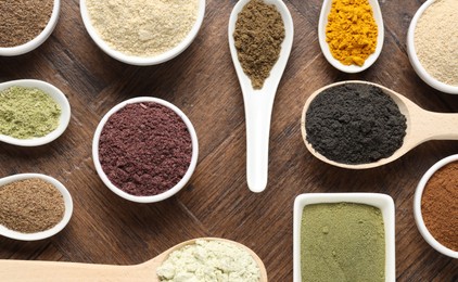 Photo of Different superfood powders in bowls and spoons on wooden table, flat lay