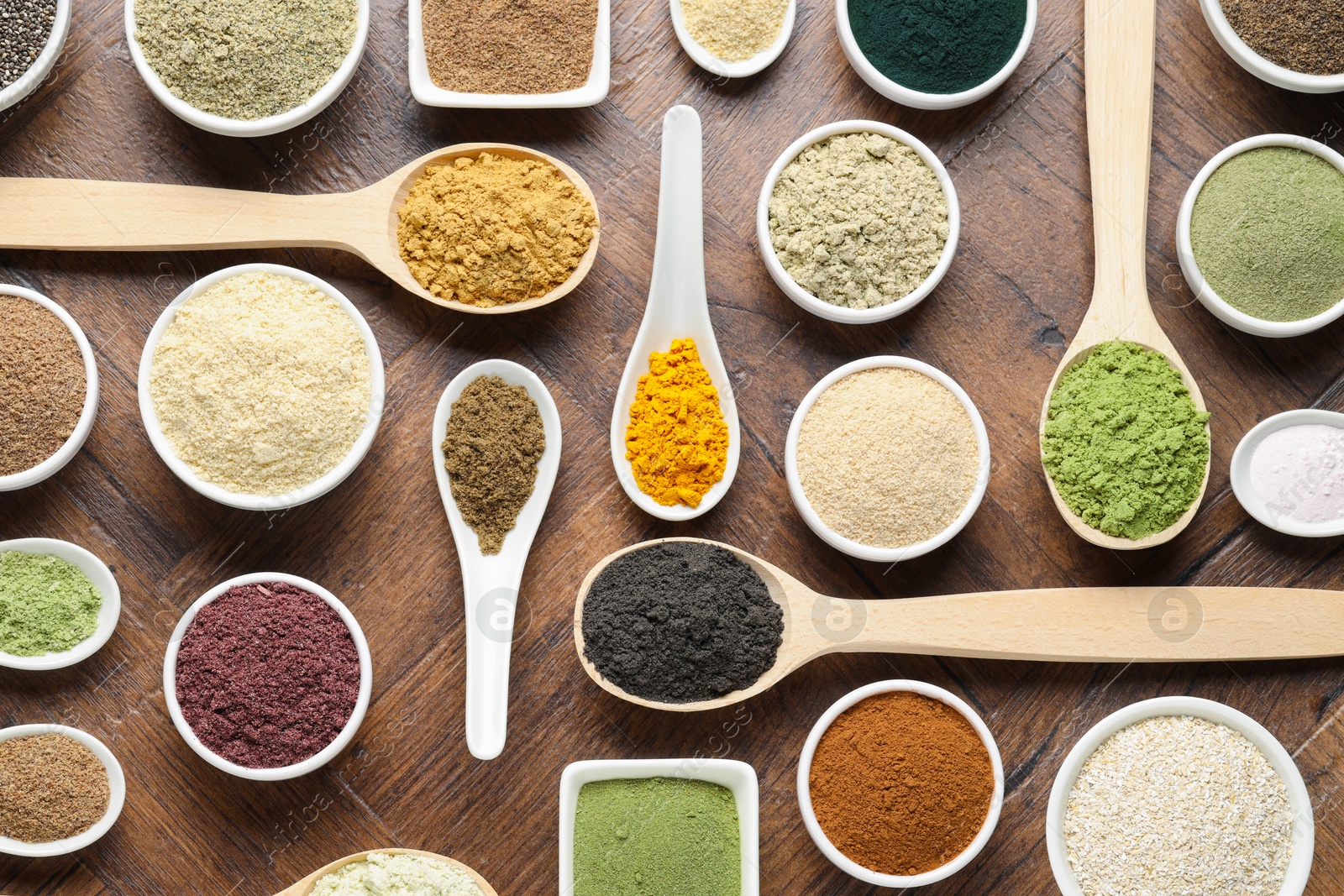 Different superfood powders in bowls and spoons on wooden table, flat lay Photo of Different superfood powders in bowls and spoons on wooden table, flat lay