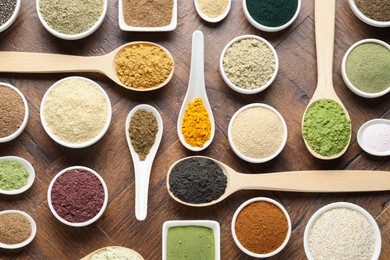 Photo of Different superfood powders in bowls and spoons on wooden table, flat lay