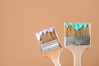 Photo of Two brushes with color paints on light brown background, closeup. Space for text