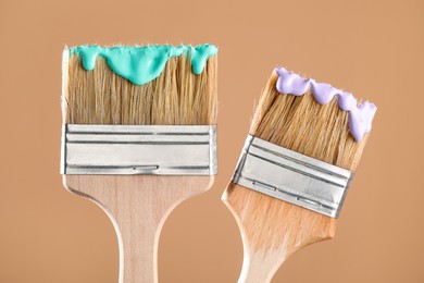 Photo of Two brushes with color paints on light brown background, closeup