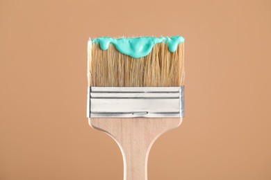 Photo of Brush with turquoise paint on light brown background, closeup