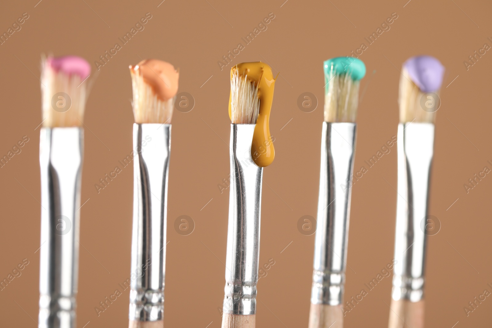Many brushes with color paints on light brown background, closeup Photo of Many brushes with color paints on light brown background, closeup