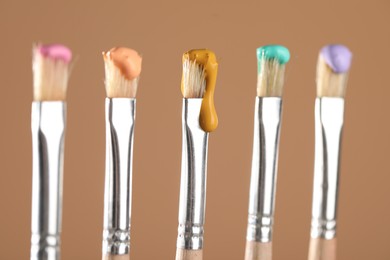 Photo of Many brushes with color paints on light brown background, closeup