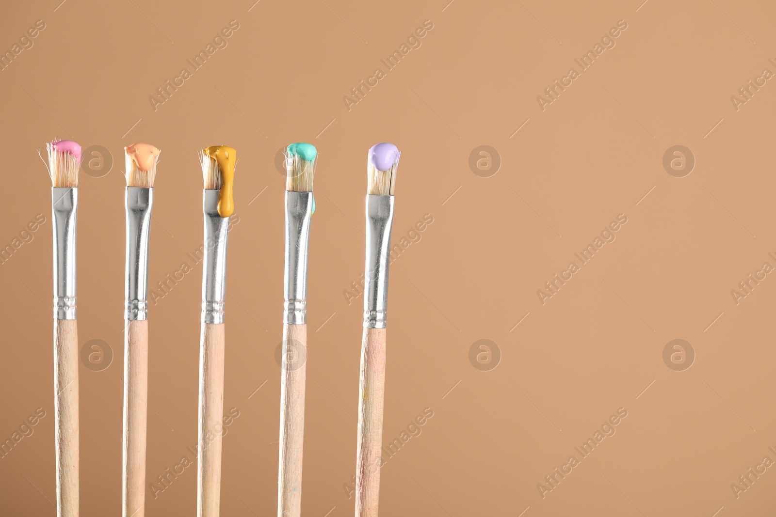 Many brushes with color paints on light brown background, closeup. Space for text Photo of Many brushes with color paints on light brown background, closeup. Space for text