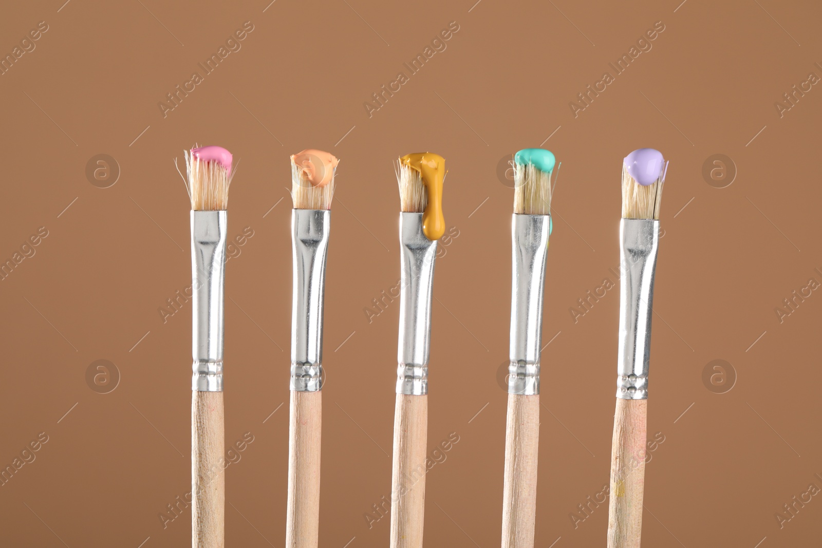 Many brushes with color paints on light brown background, closeup Photo of Many brushes with color paints on light brown background, closeup