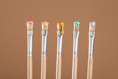 Photo of Many brushes with color paints on light brown background, closeup